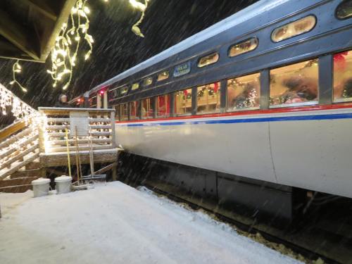 A snowy scene featuring a train car decorated with lights, parked near a wooden staircase in a winter setting.