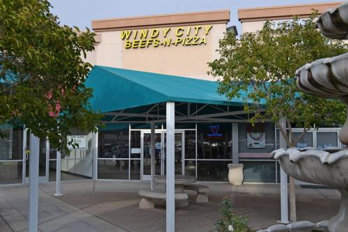 Exterior of Windy City Beefs-N-Pizza with a green awning and seating area in front.