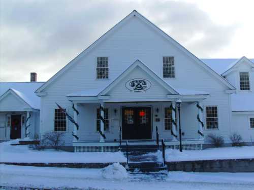 A white, snow-covered building with a welcoming entrance and festive decorations, set against a winter sky.