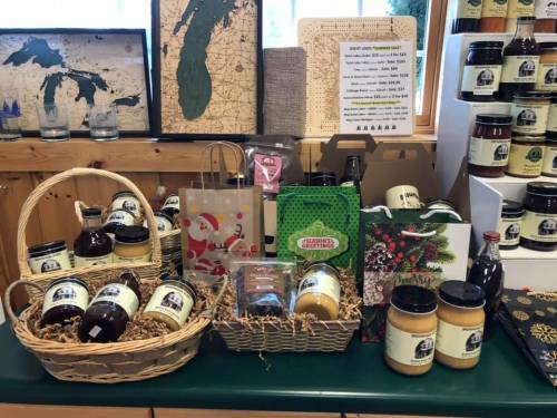 A display of various local products, including jars, baskets, and holiday-themed packaging, on a green table.