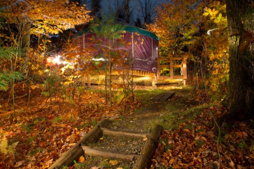 A cozy yurt surrounded by colorful autumn foliage, illuminated at night with a path leading to it.