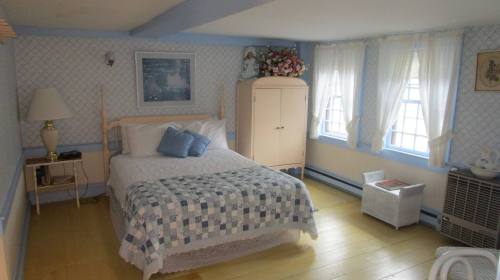 Cozy bedroom with a bed, blue and white decor, a lamp, and large windows letting in natural light.