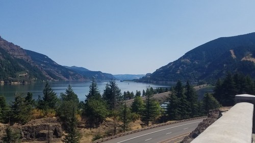 Scenic view of a river surrounded by mountains and trees under a clear blue sky.