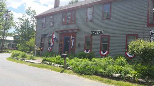 A two-story green building with red trim, featuring signs for a restaurant and tavern, decorated with patriotic bunting.