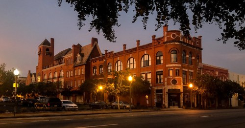 Historic brick building at dusk, featuring arched windows and decorative architecture, with streetlights illuminating the scene.
