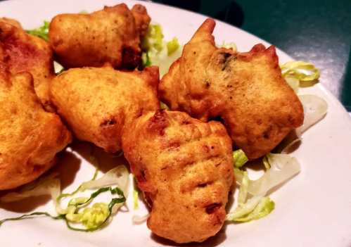 A plate of golden-brown fritters served on a bed of shredded lettuce.