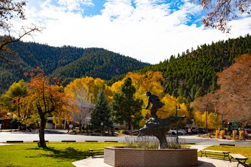 A statue of a skier on a mountain base, surrounded by colorful autumn trees and a scenic mountain backdrop.
