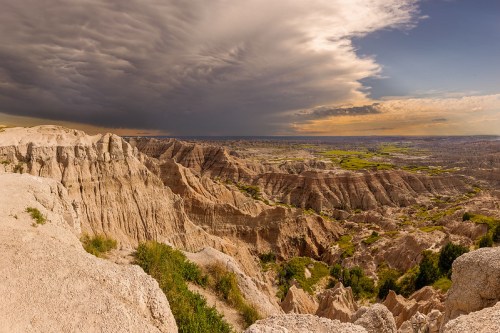 A panoramic view of rugged, layered rock formations under a dramatic sky, with green vegetation in the valley below.
