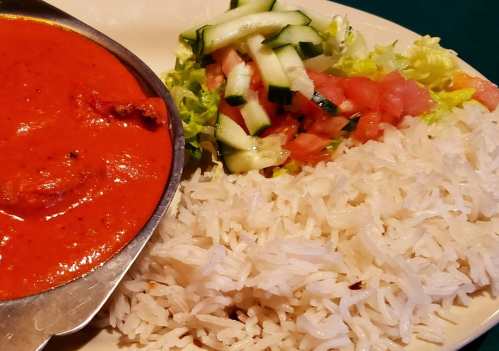 A plate featuring a serving of rice, a red curry dish, and a fresh salad with lettuce, tomatoes, and cucumbers.