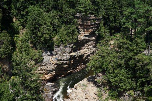 Aerial view of a rocky cliffside with a river flowing through a lush green forest.