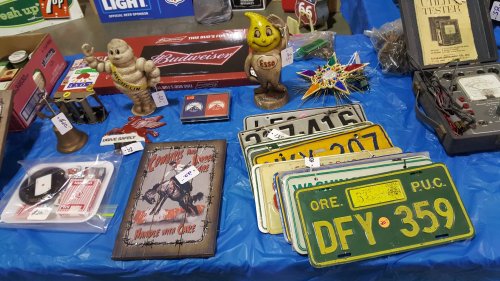 A display of vintage items including signs, license plates, and figurines on a blue tablecloth.