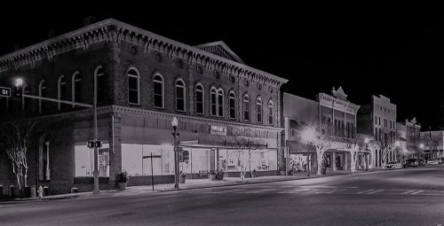 Black and white image of a quiet downtown street at night, featuring historic buildings and streetlights.