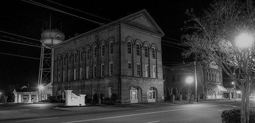 Historic brick building at night, with a water tower and streetlights illuminating the scene. Black and white photo.