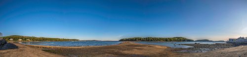 Panoramic view of a serene coastal landscape with clear blue skies, sandy shore, and distant green islands.
