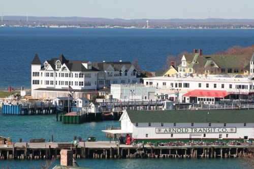 A scenic view of a waterfront with buildings, docks, and boats against a backdrop of blue water and distant hills.