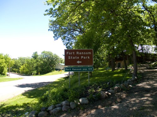 Sign for Fort Ransom State Park with directional arrow, surrounded by trees and a grassy area.