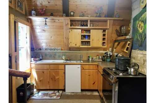 Cozy wooden kitchen with a sink, stove, and shelves filled with dishes, featuring rustic decor and natural light.