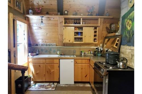 Cozy wooden kitchen with a sink, stove, and shelves filled with dishes, featuring rustic decor and natural light.
