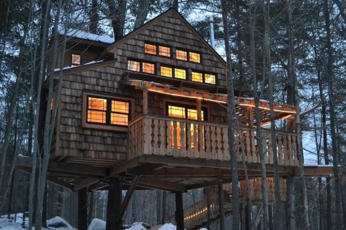A cozy treehouse with warm lights, nestled among trees in a snowy forest at dusk.