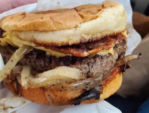 A close-up of a juicy hamburger with melted cheese, grilled onions, and a toasted bun, held in a hand.