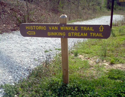 Signpost indicating directions for Historic Van Winkle Trail and Sinking Stream Trail along a gravel path.