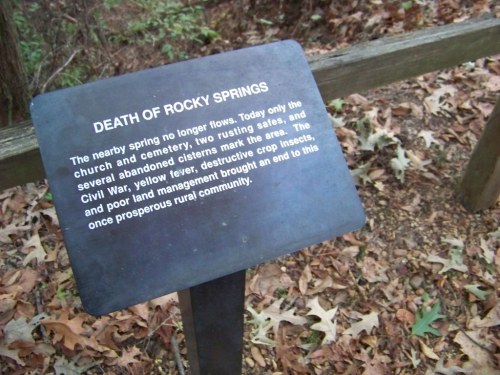 Sign titled "Death of Rocky Springs" describing the area's decline due to war, pests, and poor land management.