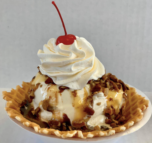 A delicious ice cream sundae in a waffle bowl, topped with whipped cream, nuts, caramel, and a cherry.
