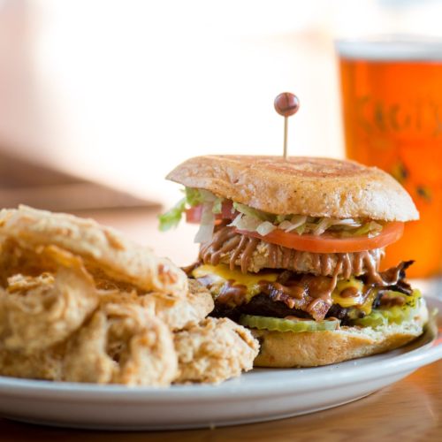 A juicy burger with lettuce, tomato, and cheese, served with crispy onion rings on a white plate.