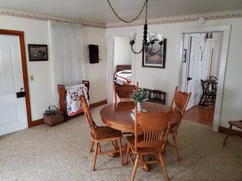 A cozy dining room with a round wooden table, chairs, and a chandelier, featuring light-colored walls and doorways.