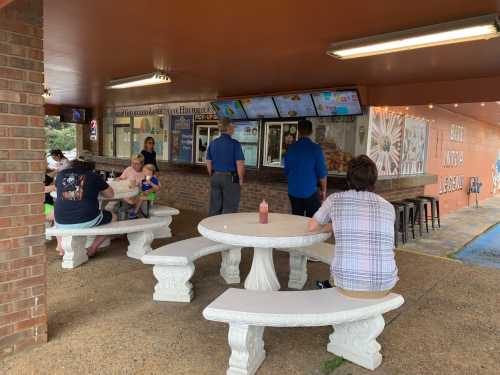 A casual outdoor dining area with people ordering food at a counter and sitting at stone tables.