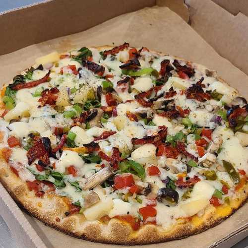 A freshly baked pizza topped with vegetables, herbs, and cheese in a cardboard box.