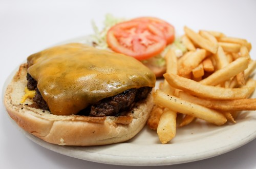 A cheeseburger with melted cheese, lettuce, and tomato, served with a side of golden French fries.