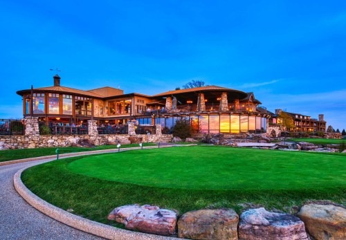A scenic view of a stone-clad clubhouse at dusk, surrounded by lush green grass and a tranquil landscape.