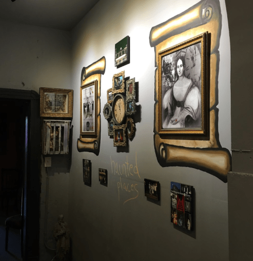 A wall decorated with framed photos and artwork, featuring a clock and the words "haunted places" in chalk.