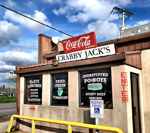 Exterior of Crabby Jack's restaurant with a Coca-Cola sign, featuring menu items like po-boys and fried green tomatoes.