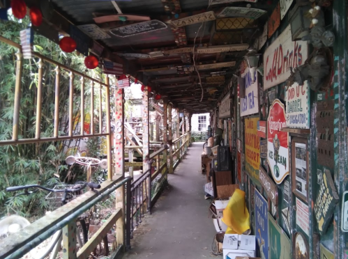 A narrow, colorful corridor lined with eclectic signs and decorations, leading to a vibrant outdoor space.