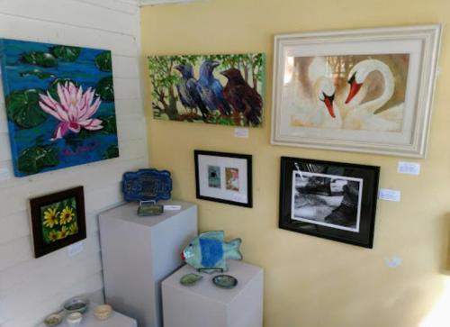 A gallery wall featuring various artworks, including paintings of flowers, birds, and swans, displayed on yellow walls.