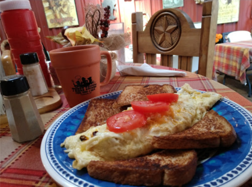 A plate of omelette with sliced tomatoes on toast, set on a checkered tablecloth in a cozy diner.