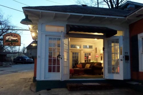 Cozy corner building with large windows, warm lighting, and a welcoming entrance, set in a quiet street at dusk.