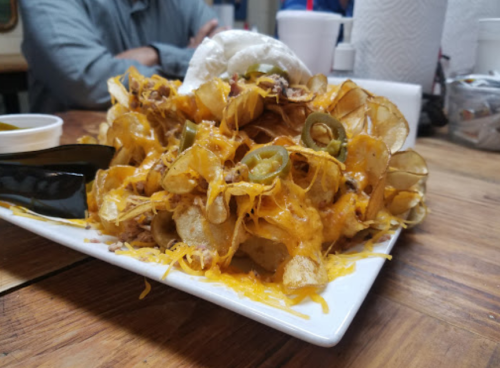 A plate of loaded nachos topped with cheese, jalapeños, and shredded meat, served on a wooden table.