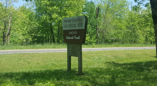 Sign for Pioneer Cemetery Historical Site in Ouachita, surrounded by greenery and visible from a nearby road.