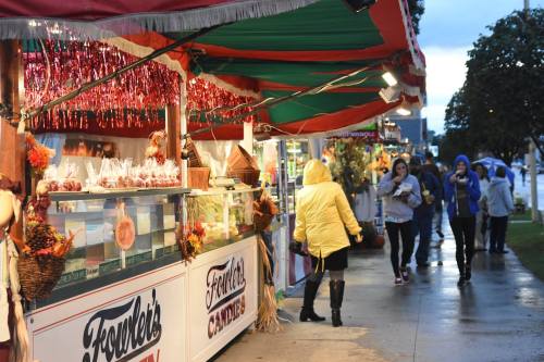 A rainy street scene with colorful market stalls and people walking, some in raincoats, enjoying the festive atmosphere.