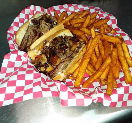 A basket of pulled beef sandwiches with sautéed vegetables and a side of crispy sweet potato fries.