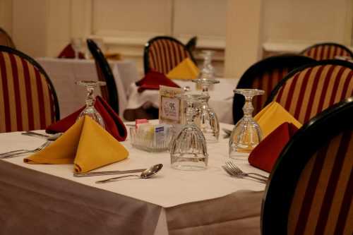 Elegant dining setup with white tablecloths, red and yellow napkins, and glassware on polished tables.