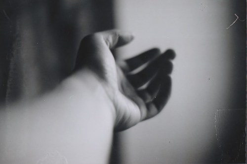 A close-up of an outstretched hand reaching towards the viewer, set against a blurred background.