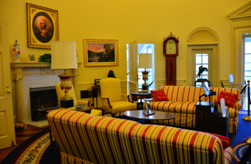 A cozy room with striped sofas, a fireplace, a clock, and artwork on the walls, featuring warm yellow tones.