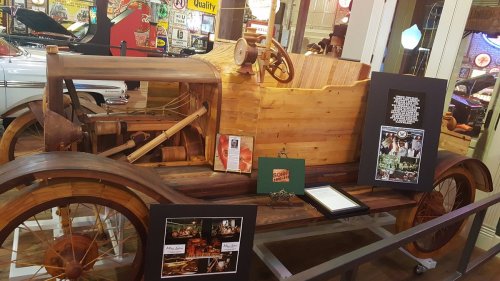 A vintage wooden car display with framed photos and memorabilia in a museum setting.