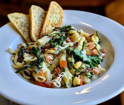 A bowl of pasta with vegetables and cheese, served with slices of garlic bread on the side.