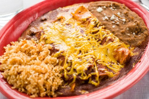 A vibrant plate of enchiladas topped with cheese, accompanied by rice and refried beans.