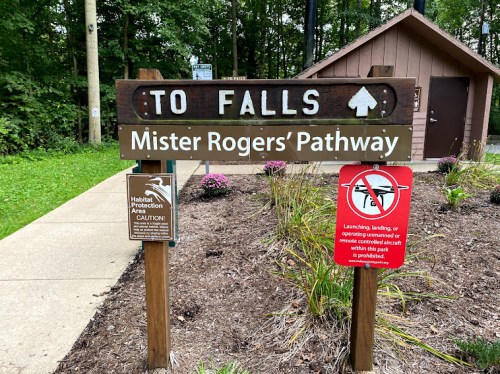 Sign directing to Falls and Mister Rogers' Pathway, with caution signs about habitat protection and no launching or landing.